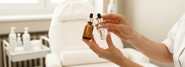 Esthetician holding two serum bottles in a spa — natural vs synthetic vitamins in skincare products.