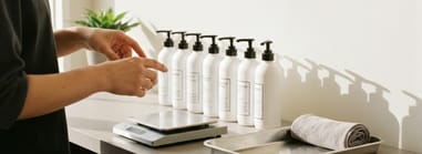 Person preparing salon backbar bottles with pumps, using a digital scale for accurate measuring.
