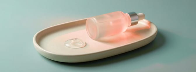 Minimal skincare serum bottle with dropper on a ceramic tray with gel texture sample on a soft blue background.
