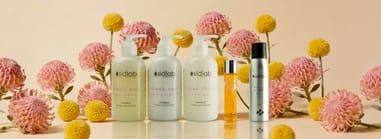 SidLab Haircouture products displayed among pink and yellow flowers, showcasing sleek shampoo, conditioner, and styling formulas.