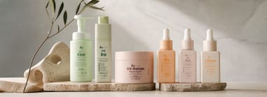 IKI Skincare line — Kirei cleanser, Iro emulsion, Gaman balm, and three serums on stone platforms with an olive branch.