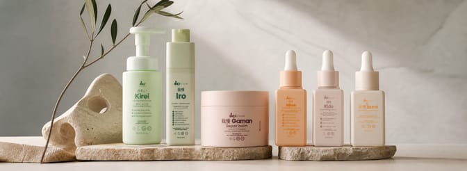 IKI Skincare line — Kirei cleanser, Iro emulsion, Gaman balm, and three serums on stone platforms with an olive branch.